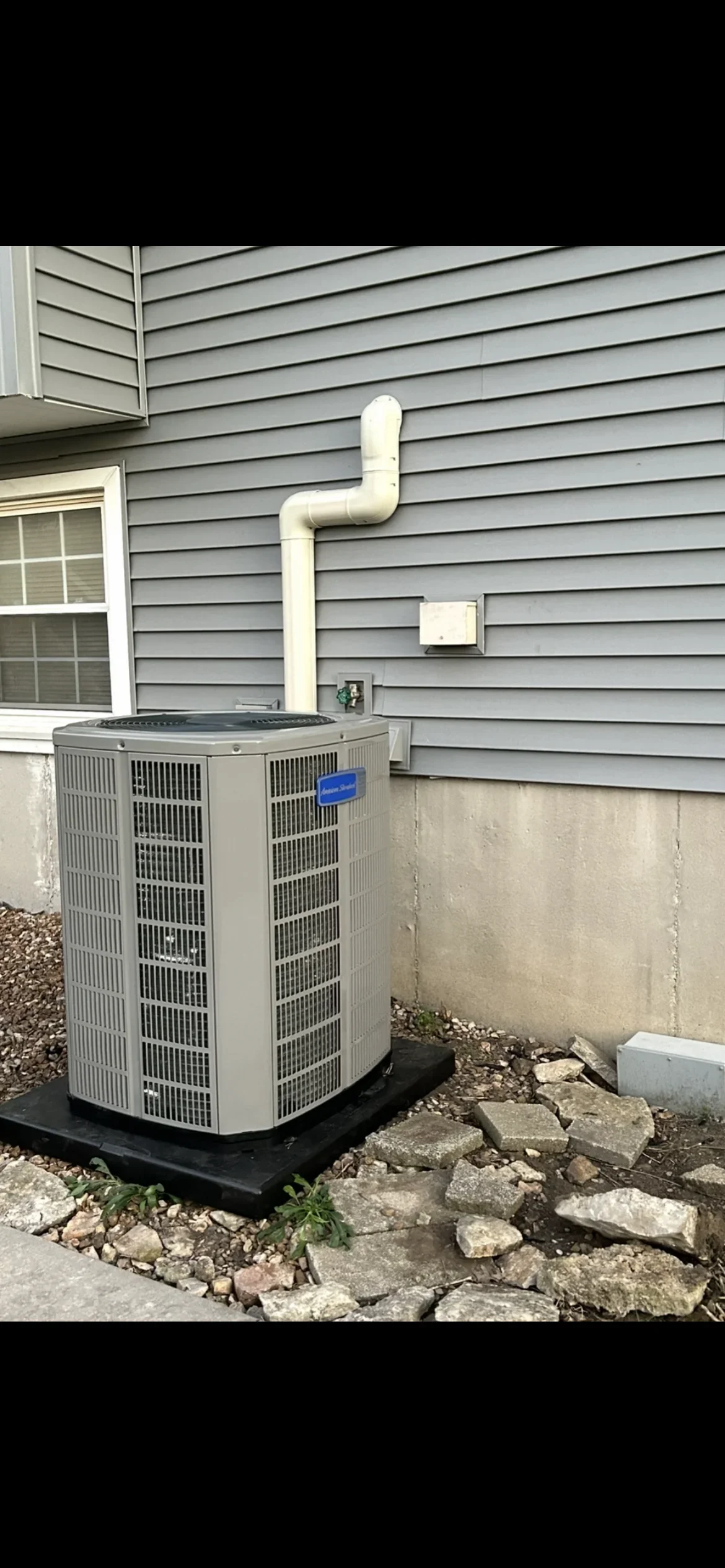 Installed AC condenser unit with white PVC piping on concrete pad against vinyl siding