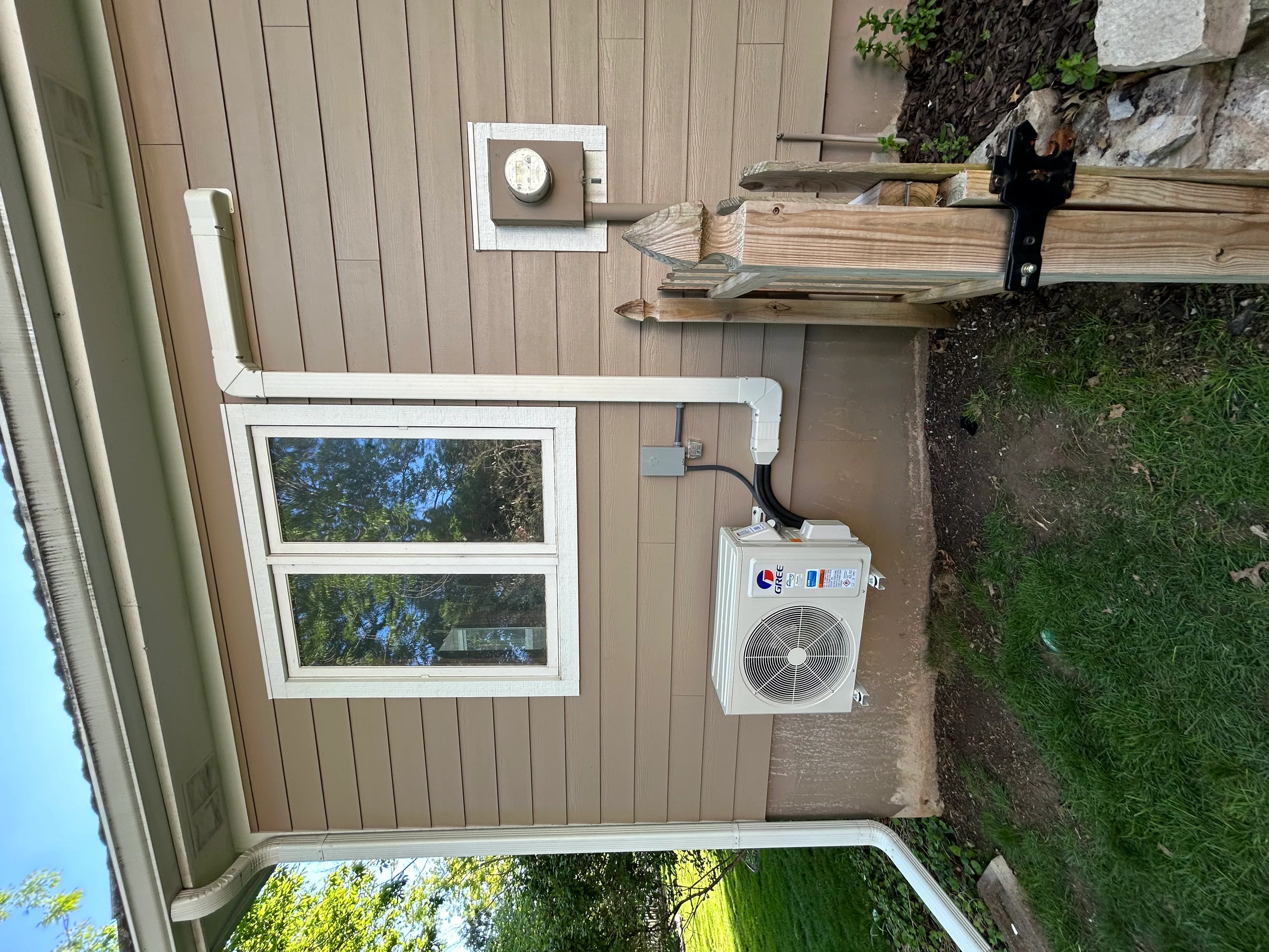 Exterior mini-split HVAC unit with white compressor, refrigerant lines, and drain installation on wood siding