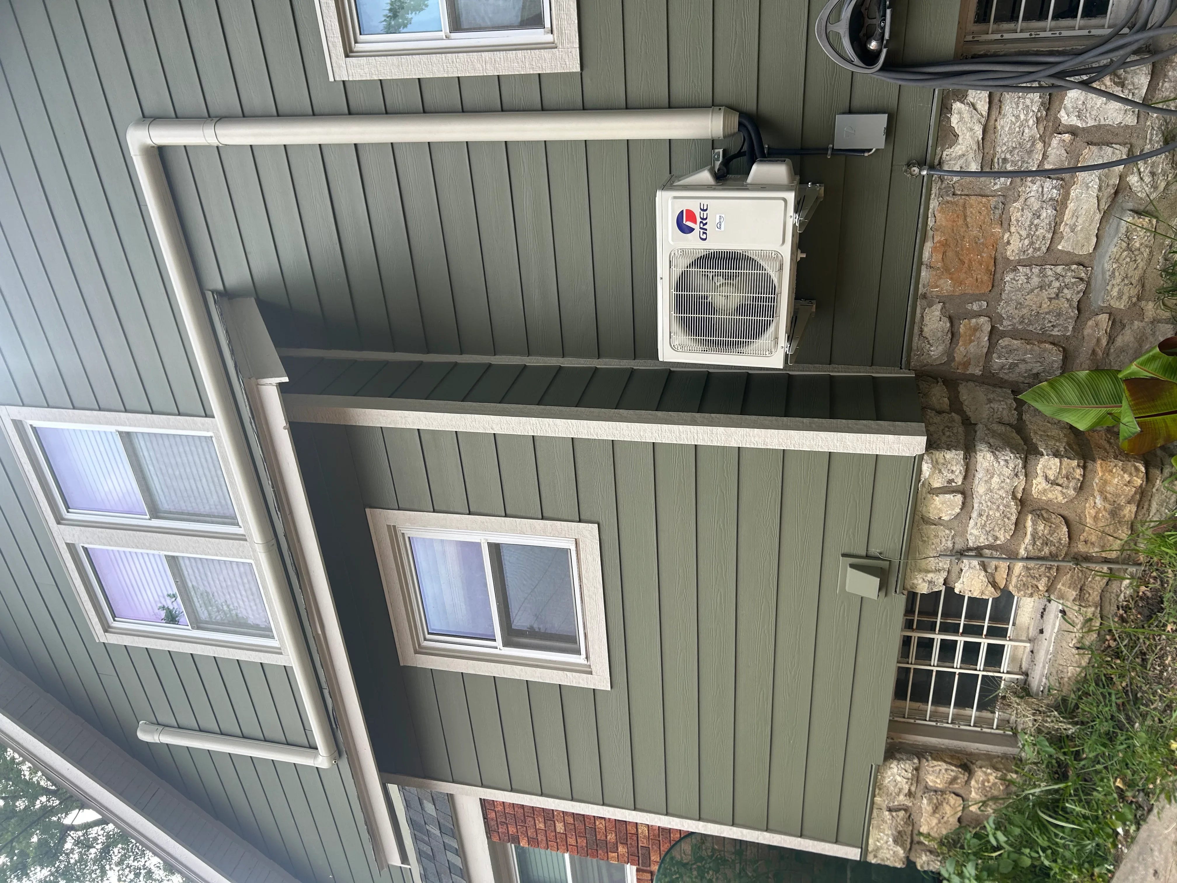 Exterior mini-split heat pump unit mounted on metal siding with refrigerant lines and drain installation