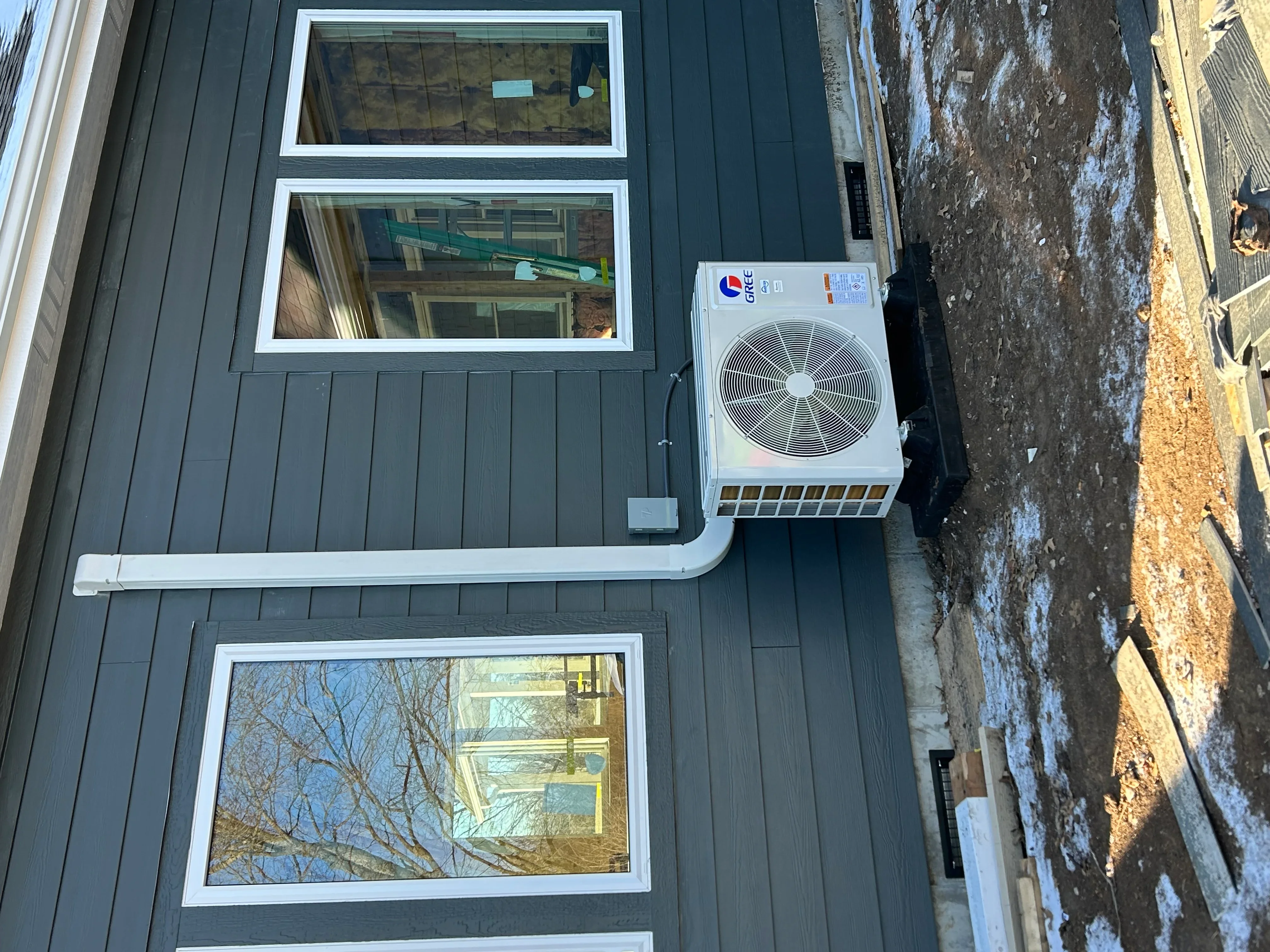 Ductless mini-split heat pump with outdoor condenser and white-trimmed indoor units on metal siding