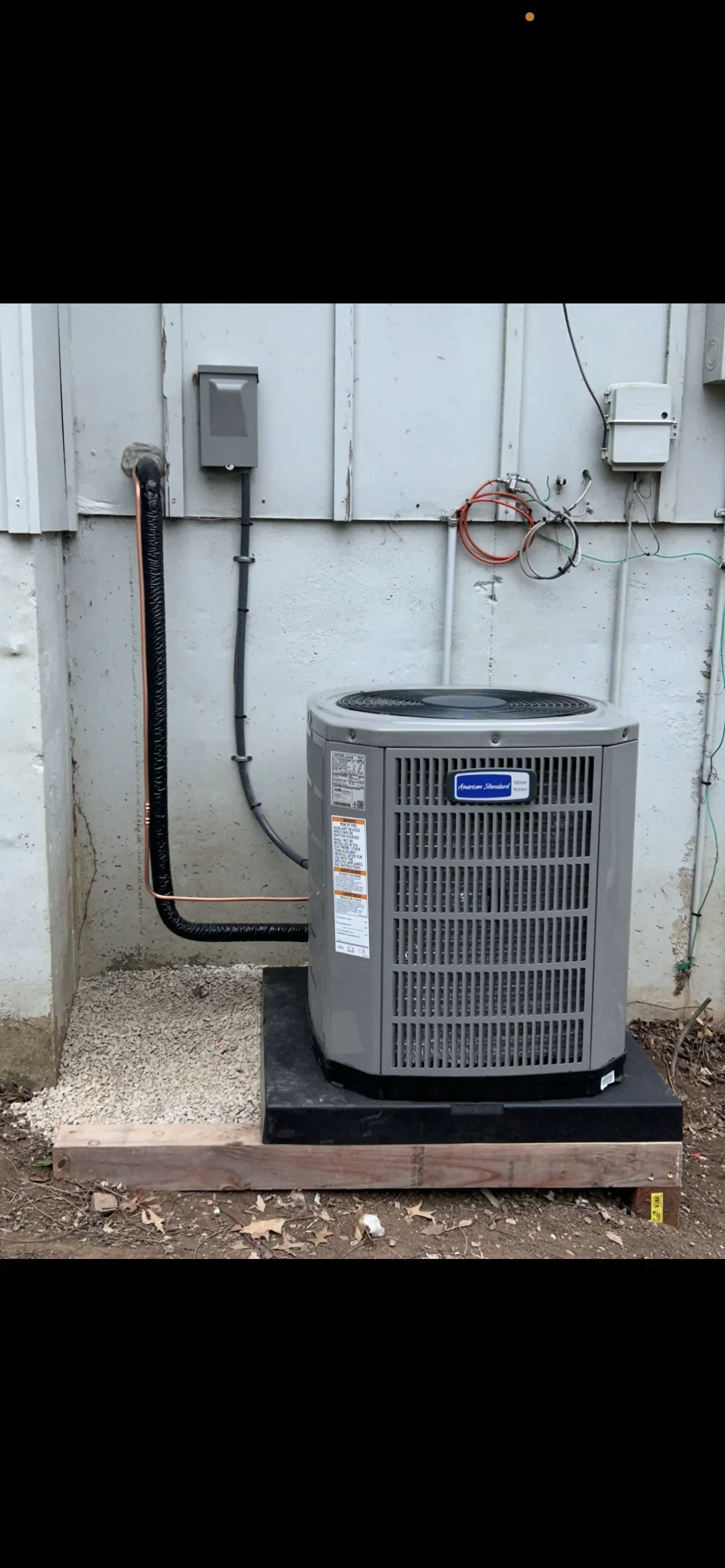 Gray AC condenser unit on concrete pad with copper refrigerant lines and electrical connections