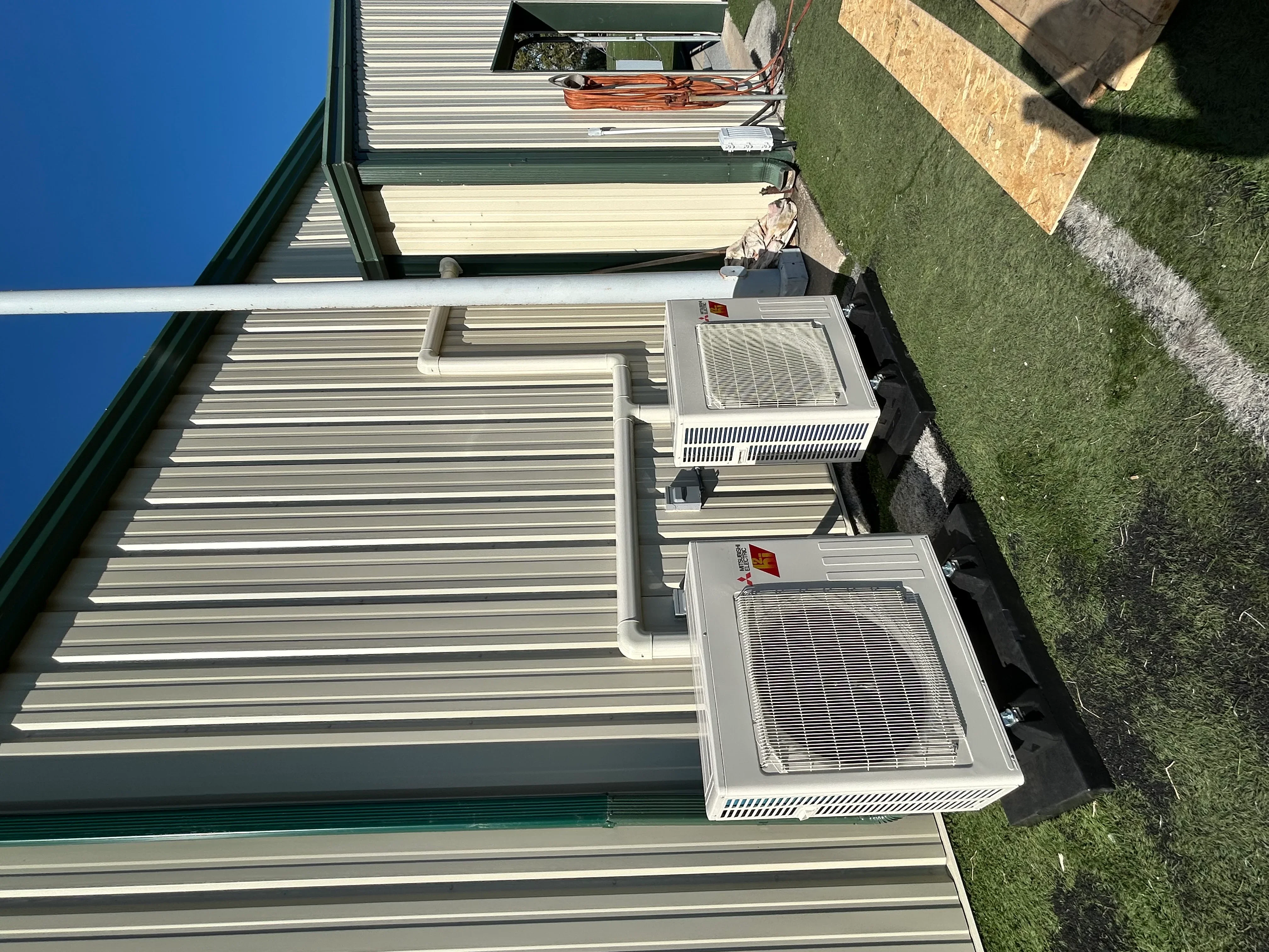 Two white through-wall AC units installed on metal siding exterior with grilles and electrical connections
